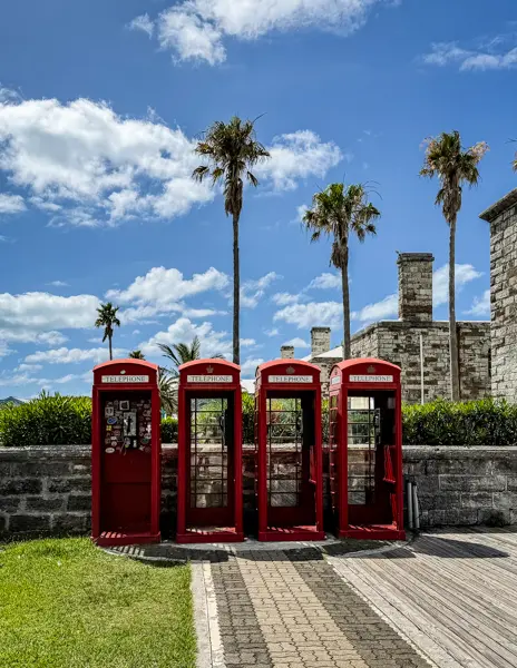 Red British telephone booths lined up beneath palm trees and a blue sky in Bermuda.