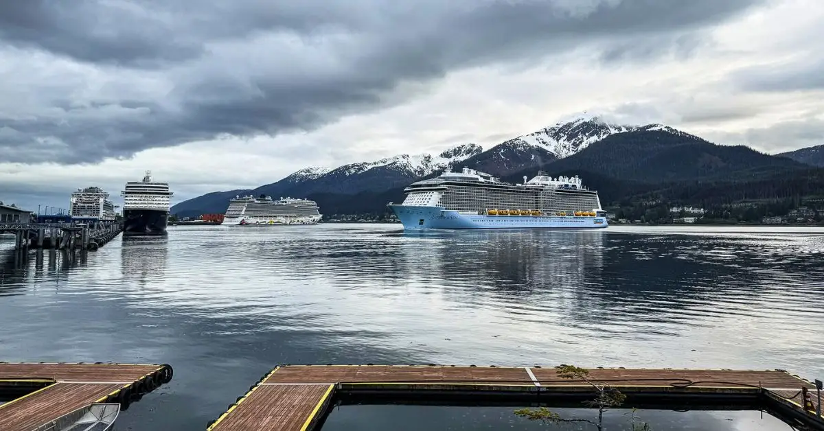 featured image: Cruise ship pulling away from an Alaska port beneath snow-covered mountains, featured in a guide to cruise ship facts you might not know.
