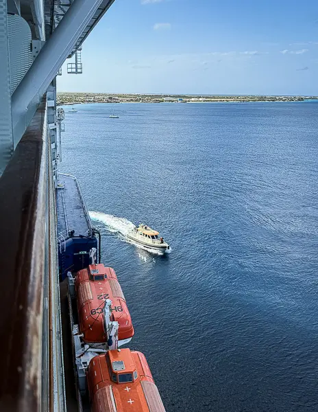 Harbor pilot boat traveling alongside a cruise ship near port.