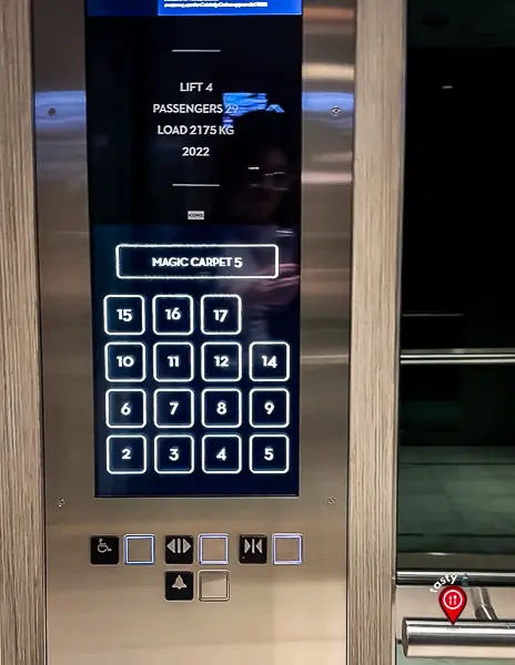 Close-up of a cruise ship elevator control panel with illuminated floor buttons. The number 13 is missing, jumping from floor 12 to 14, and a screen above reads “Magic Carpet 5.”