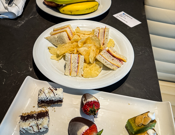 NCL Haven daily snacks with club sandwiches, potato chips, chocolate-covered strawberries, and small desserts