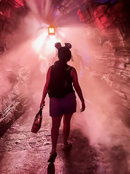 Kathy walking through a fog-filled tunnel with red lighting inside Villains Grove at Oogie Boogie Bash.