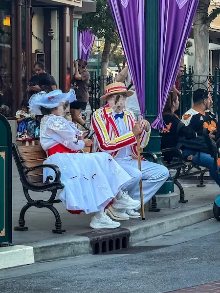 wo Oogie Boogie Bash guests dressed as Mary Poppins and Bert sitting on a bench at Disney California Adventure.