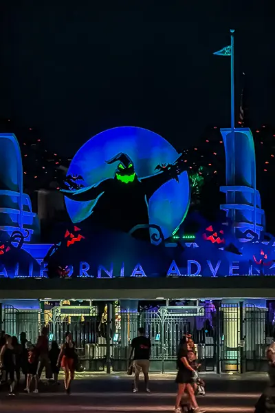 Giant Oogie Boogie decoration glowing green in front of the Disney California Adventure entrance at night.