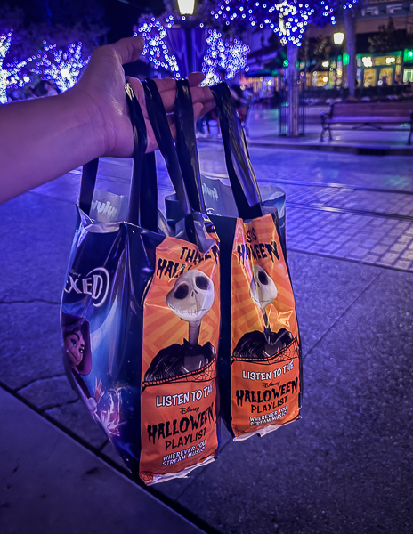 Oogie Boogie Bash treat bags and orange Jack Skellington Halloween treat bags held up at night in Disney California Adventure.