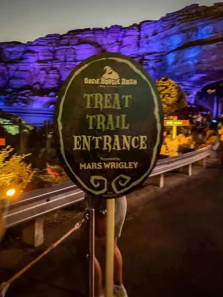 Treat trail entrance sign at Oogie Boogie Bash in Disney California Adventure, with colorful nighttime lighting in the background.