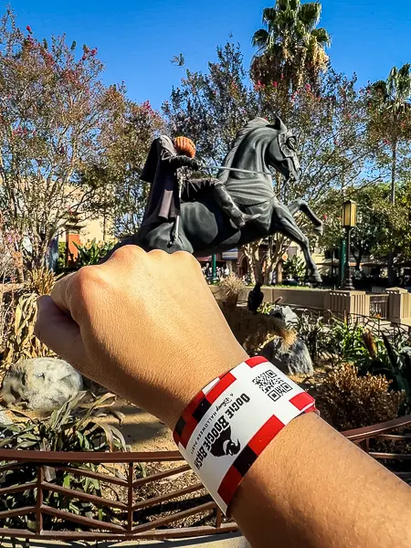 Oogie Boogie Bash wristband held up in front of the Headless Horseman statue at Disney California Adventure.